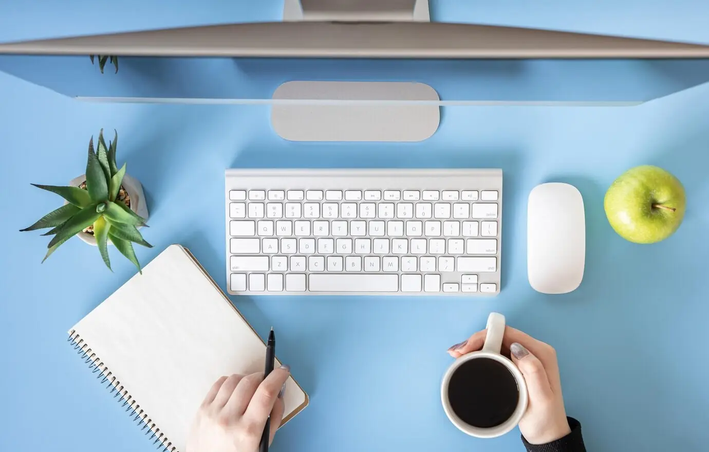 Draufsicht auf weibliche Hände, die am Computer arbeiten, vor blauem Hintergrund.